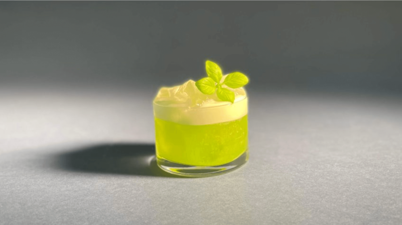 Auf dem Bild steht ein Gin Basil Smash in einem kleinen Cocktailglas. Nach Rezept dekoriert mit Basilikum und viel Eiswürfeln.